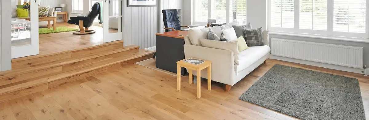 A modern living room with professionally installed laminate flooring, a beige sofa, a small side table, a gray rug, and large windows with white shutters in Green Bay, WI